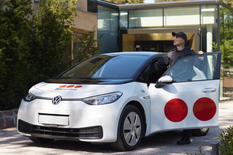 Securitas security professional exiting Securitas branded vehicle that is parked outside a building looking upwards.