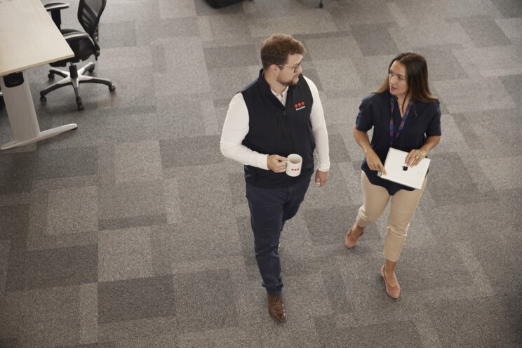 Two Securitas Security Professionals (a man and a woman) are walking and talking together in a Securitas office setting, discussing Security Solutions.  
