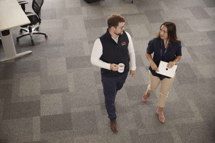 Two Securitas Security Professionals (a man and a woman) are walking and talking together in a Securitas office setting, discussing Security Solutions.